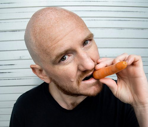 Künstler Norbert Ortner mit einer Karotte als Zigarre im Munde