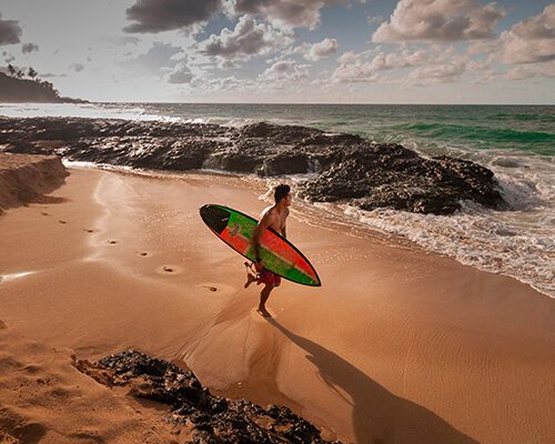Mann mit Surfbrett an einem Strand mit Meer im Hintergrund