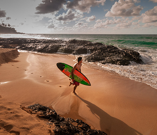 Mann mit Surfbrett an einem Strand mit Meer im Hintergrund